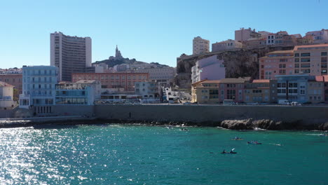 Kayaks-along-a-coastal-road-in-Marseille-with-Notre-Dame-church-in-background